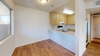 Located at 923 Alturas Road in Fallbrook, California, this single-floor unit offers a practical and well-organized layout across several distinct living areas. The main living space features warm wood-look laminate flooring that runs throughout, complemented by neutral wall tones and a textured ceiling. A large window allows natural light to fill the room, creating a bright and open atmosphere, while a classic six-panel front door provides a clean entryway.

The kitchen is positioned adjacent to the living and dining area, separated by a peninsula countertop that doubles as a convenient breakfast bar. Light wood cabinetry offers ample storage, and the kitchen is equipped with a white range and refrigerator. Recessed lighting above the workspace ensures the area remains well-lit.

The bedrooms are carpeted for comfort and feature neutral walls with natural light provided by windows that offer views of surrounding greenery. Each bedroom includes closet space, with one room showcasing a sliding door closet with a full-width rod and an additional built-in cabinet for extra storage.

The bathroom is finished with tile flooring and includes a single-sink vanity with wood cabinetry, a toilet, and a combination tub and shower unit fitted with a handheld showerhead and a safety grab bar, offering both functionality and accessibility.