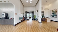 This generously sized single-floor amenity center offers a comprehensive suite of community spaces designed for both comfort and functionality. The grand lobby entrance sets the tone with soaring ceilings, large black-framed glass doors, and warm hardwood-style flooring that flows throughout the space, creating a bright and welcoming first impression.

The open lounge area is a central gathering point, furnished with plush sofas, leather chairs, a large wall-mounted TV, and distinctive pendant lighting. Floor-to-ceiling windows and glass doors provide abundant natural light and views to an outdoor pool area beyond. Adjacent to the lounge is a dedicated coffee bar nook, outfitted with dark cabinetry, countertops, and a professional-grade coffee machine, ideal for residents on the go.

The fitness center is well-appointed with high ceilings, large windows, and a full array of cardio and strength equipment including treadmills, ellipticals, a StairMaster, stationary bikes, and cable machines. A motivational "Work For It" wall mural reinforces the space's energetic atmosphere.

A spacious mail room features rows of individual resident mailboxes, decorative wall art, and tile flooring. Private office and meeting rooms with glass-panel walls round out the facility, offering quiet, professional settings for focused work or consultations.
