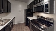 This single-story unit offers a practical and well-organized layout, as revealed by the 3D floor plan. The kitchen is efficiently designed and equipped with dark cabinetry, white countertops, and a full suite of stainless steel appliances, including a refrigerator, electric range, and over-the-range microwave. Light wood-look vinyl flooring runs through the kitchen and extends into the main living area, providing a cohesive, easy-to-maintain surface throughout the common spaces.

The living area is open and spacious, featuring a textured ceiling, neutral-toned walls, and a built-in closet with panel doors. A window allows natural light to filter in, and the room connects seamlessly to the kitchen, enhancing the open feel. Bedroom spaces are carpeted and generously sized, each benefiting from windows that bring in views of surrounding greenery. One bedroom includes access to a walk-in closet and an additional door to the hallway. The bathroom is clean and modern, featuring a dark vanity with a white countertop, large mirror, and wood-look flooring that ties in with the rest of the unit.