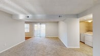 This single-floor residence offers a thoughtfully laid-out interior with a neutral color palette and a variety of functional spaces. The expansive living area is carpeted throughout and anchored by a classic fireplace, creating a warm and inviting atmosphere. Large sliding glass doors lead to an outdoor space, flooding the room with natural light and providing easy access to the exterior. Structural beam detailing and a textured ceiling add architectural character to the open layout.

The galley-style kitchen is efficiently designed with rich dark cabinetry, light countertops, hardwood-style flooring, and stainless steel appliances including a refrigerator and range, offering ample storage and prep space.

The bedrooms are generously sized, each with plush carpeting, ceiling fans with light fixtures, and windows that bring in natural light. The primary bedroom features direct access to an en-suite bathroom equipped with a bathtub and shower combination. A second full bathroom with hardwood-style flooring and a tub-shower unit serves the remaining rooms.

A dedicated in-unit laundry area with a full-size washer and dryer, complete with overhead wire shelving, adds everyday convenience. Throughout the space, consistent finishes and a clean, understated aesthetic create a comfortable and functional living environment.
