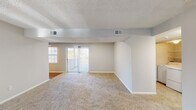 This single-floor residence offers a thoughtfully laid-out interior with a neutral color palette and a variety of functional spaces. The expansive living area is carpeted throughout and anchored by a classic fireplace, creating a warm and inviting atmosphere. Large sliding glass doors lead to an outdoor space, flooding the room with natural light and providing easy access to the exterior. Structural beam detailing and a textured ceiling add architectural character to the open layout.

The galley-style kitchen is efficiently designed with rich dark cabinetry, light countertops, hardwood-style flooring, and stainless steel appliances including a refrigerator and range, offering ample storage and prep space.

The bedrooms are generously sized, each with plush carpeting, ceiling fans with light fixtures, and windows that bring in natural light. The primary bedroom features direct access to an en-suite bathroom equipped with a bathtub and shower combination. A second full bathroom with hardwood-style flooring and a tub-shower unit serves the remaining rooms.

A dedicated in-unit laundry area with a full-size washer and dryer, complete with overhead wire shelving, adds everyday convenience. Throughout the space, consistent finishes and a clean, understated aesthetic create a comfortable and functional living environment.