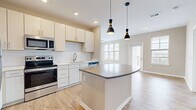 This well-appointed single-story residence offers a thoughtfully designed layout comprising one bedroom and three bathrooms across a generously sized floor plan. The open-concept kitchen and living area serves as the heart of the home, featuring light-toned cabinetry, a classic white subway tile backsplash, and a full suite of stainless steel appliances. A curved kitchen island with a gray quartz-style countertop provides additional prep space and casual seating, accented by a pair of modern pendant lights overhead. Light wood-look flooring runs throughout the main living areas, enhancing the bright, airy atmosphere. The living area benefits from multiple windows that invite natural light and offer outdoor views. The spacious primary bedroom is carpeted for comfort and includes large windows framing scenic exterior views, with a ceiling fan adding functionality. The en-suite bathroom features an elongated vanity with white countertops and a walk-in glass-enclosed shower finished in large-format marble-patterned tile. Additional bathrooms maintain the same clean, modern aesthetic with warm wood-tone accents and quality fixtures. Neutral warm-beige walls and white trim carry consistently throughout, giving the entire residence a cohesive, contemporary feel.