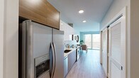 This thoughtfully designed single-floor residence offers a seamless blend of modern aesthetics and functional living. The galley-style kitchen is a standout feature, outfitted with stainless steel appliances including a French door refrigerator, electric range, built-in microwave, and dishwasher. Sleek two-tone cabinetry — combining white upper cabinets with warm wood-grain lower units — frames a geometric tile backsplash, while light wood-look flooring runs throughout the space, tying each room together cohesively.

The open living and dining area is bathed in natural light, courtesy of large sliding glass doors that lead directly to a private balcony with open views of the surrounding treetops. The living room provides ample space for relaxed seating arrangements, complemented by neutral walls and recessed lighting.

The bedroom is generously proportioned, offering direct sightlines to the living area and featuring a dedicated walk-in closet with built-in shelving — a practical and well-organized storage solution. The full bathroom is clean and contemporary, finished with marble-style tile flooring, a soaking tub with shower, and a wood-accented vanity. Throughout, the space maintains a bright, airy ambiance with a consistent modern design language.