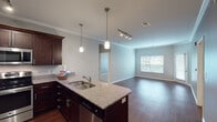 This single-floor residence at 9561 N Ambassador Dr in Kansas City, MO offers a cohesive and well-finished interior design throughout. The open-concept kitchen and living area serves as the heart of the unit, where rich dark cabinetry pairs with granite countertops and a peninsula island illuminated by pendant lighting. Stainless steel appliances, including a refrigerator, range, and microwave, complete the functional kitchen. Crown molding and track lighting add refined detail to the living area, which features hardwood-style flooring and a window that brings in natural light.

The bedrooms are carpeted and neutral in tone, with ceiling fans and windows providing ventilation and light. One bedroom is notably spacious, while an additional room offers flexible use. Two bathrooms serve the unit: one features a double-sink vanity with granite countertops and a tub-shower combination, while the other includes a single vanity and a glass-enclosed tiled walk-in shower. Both bathrooms continue the dark cabinetry theme. In-unit laundry access is also visible, adding everyday convenience to this thoughtfully designed space.