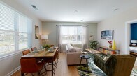 Located at 2020 Morton St in Charlotte, NC, this single-floor residence showcases a thoughtfully designed open-concept layout with contemporary finishes throughout. Light-toned hardwood-style flooring runs through the main living areas, complementing the neutral color palette and creating a cohesive, modern aesthetic.

The kitchen serves as a central hub, featuring a large island with a built-in sink, seating for two, and elegant globe pendant lighting overhead. Light wood cabinetry pairs with a white tile backsplash, and stainless steel appliances — including a refrigerator, range, and microwave — complete the space. Natural light from nearby windows adds brightness to the area.

The open living and dining area offers generous space for both relaxing and entertaining. Multiple windows allow abundant natural light and outdoor views, while the layout comfortably accommodates both a full seating arrangement and a dining table.

The primary bedroom features a striking teal accent wall, plush carpeting, and an en-suite bathroom equipped with a glass-enclosed shower, a wood-toned vanity, and a walk-in closet with built-in shelving. A second bedroom is bright and airy, with large windows and soft carpeting.

Additional features include a mudroom-style entry with built-in shelving, recessed lighting, and practical storage throughout.