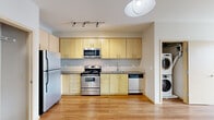 Located at 1450 N Prescott St in Portland, Oregon, this single-floor, 3-bedroom, 2-bathroom residence offers a clean, modern design with a practical and efficient layout. The open-concept kitchen is a standout feature, outfitted with light maple cabinetry extending to the ceiling, stainless steel appliances including a range, microwave, dishwasher, and refrigerator, and a continuous countertop with an integrated sink. Track lighting overhead and warm hardwood-style flooring add to the kitchen's bright, contemporary feel. A stacked washer and dryer unit is conveniently located just off the kitchen. The living area continues the hardwood-style flooring and features a wall-mounted mini-split HVAC unit, offering climate control, along with large windows and a sliding glass door that invite natural light and provide outdoor views. The three bedrooms are carpeted and offer a quiet, comfortable retreat, each with closets featuring sliding or hinged doors. The spacious primary bedroom provides ample room and natural light. Both bathrooms are finished with tile flooring and include a full tub-shower combination. Neutral wall tones throughout create a cohesive, move-in-ready atmosphere suited for a variety of living arrangements.