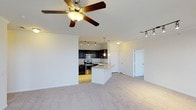 This single-floor residence in Frisco offers an open-concept layout that integrates the living and kitchen areas into one cohesive, functional space. The living area is finished with plush neutral carpeting and features a ceiling fan, contributing to a comfortable and well-ventilated environment. Track lighting accents the space, providing flexible illumination throughout.

The kitchen is a standout feature, appointed with dark espresso cabinetry that creates a striking contrast against the lighter surroundings. Stainless steel appliances, including a range and microwave, add a modern, polished touch. A central island with a light-toned countertop and pendant lighting overhead serves as both a workspace and a casual dining or gathering spot. The island also houses a sink, enhancing its functionality.

The open flow between the kitchen and living area gives the space an expansive, airy feel. A doorway visible from the main living area leads to additional rooms, suggesting a thoughtful and practical floor plan. Overall, the space presents a clean, contemporary aesthetic with a neutral palette that offers a versatile backdrop for personalization.