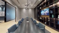 Located at 1205 Worcester St in Natick, Massachusetts, this single-floor amenity space exemplifies contemporary design with a refined, upscale aesthetic. The expansive lounge is anchored by a dramatic floor-to-ceiling gold mosaic tile fireplace wall, serving as a striking focal point that sets the tone for the entire space. Surrounding the fireplace, a carefully curated seating area features white curved armchairs, a rounded coffee table, and a richly patterned blue-and-white area rug, all resting on wide-plank light hardwood flooring. Ambient cove lighting and a sculptural globe chandelier lend warmth and elegance to the coffered ceiling above. An adjoining lounge area continues the sophisticated palette, with a white sofa, navy accent pillows, brass-accented floor lamps, and curated blue abstract artwork adorning the walls. A full-height mirror enhances the sense of depth throughout. One of the most impressive architectural features is the expansive curtain wall of floor-to-ceiling windows that lines an entire corridor, flooding the space with abundant natural light and offering sweeping views of a landscaped courtyard and the surrounding community. Softly upholstered teal swivel chairs positioned along the window wall invite relaxed seating with an outdoor connection. Throughout, the design strikes a balance between modern sophistication and welcoming comfort.