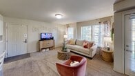 This single-floor residence offers a practical and comfortable layout across two bedrooms and two bathrooms. The living room serves as the heart of the home, featuring plush wall-to-wall carpeting, multiple windows fitted with blinds that allow for ample natural light, and neutral-toned walls that create a warm, welcoming ambiance. The kitchen is well-equipped with warm wood cabinetry, stainless steel appliances including a range, over-the-range microwave, and a side-by-side refrigerator, all complemented by laminate countertops and easy-care tile flooring. A peninsula counter provides additional workspace and a casual dining option. The generously sized primary bedroom features soft carpeting, a ceiling fan, and a window that brings in natural light. It is served by a private bathroom with a wood-vanity, marble-style countertop, and tile flooring, with direct access to a walk-in closet offering built-in shelving. The second bedroom is equally comfortable with carpeted floors and a ceiling fan. A dedicated laundry area with washer/dryer hookups adds everyday convenience. Throughout, the consistent use of neutral tones and practical finishes creates a cohesive and livable space.