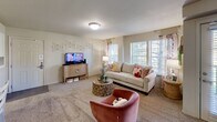 This single-floor residence offers a practical and comfortable layout across two bedrooms and two bathrooms. The living room serves as the heart of the home, featuring plush wall-to-wall carpeting, multiple windows fitted with blinds that allow for ample natural light, and neutral-toned walls that create a warm, welcoming ambiance. The kitchen is well-equipped with warm wood cabinetry, stainless steel appliances including a range, over-the-range microwave, and a side-by-side refrigerator, all complemented by laminate countertops and easy-care tile flooring. A peninsula counter provides additional workspace and a casual dining option. The generously sized primary bedroom features soft carpeting, a ceiling fan, and a window that brings in natural light. It is served by a private bathroom with a wood-vanity, marble-style countertop, and tile flooring, with direct access to a walk-in closet offering built-in shelving. The second bedroom is equally comfortable with carpeted floors and a ceiling fan. A dedicated laundry area with washer/dryer hookups adds everyday convenience. Throughout, the consistent use of neutral tones and practical finishes creates a cohesive and livable space.