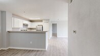 This single-floor, 2-bedroom, 3-bathroom residence offers a thoughtfully designed layout that maximizes functionality and comfort. The open-concept living area seamlessly connects the dining room, kitchen, and living room, creating a bright and cohesive space finished with light wood-style flooring throughout. The kitchen is equipped with white shaker cabinetry, stone-look countertops, stainless steel appliances including a refrigerator and electric range, and a peninsula that provides additional counter space and a natural divider between the kitchen and living areas. The living room features a ceiling fan and sliding glass doors that open onto a private balcony with outdoor views. Both bedrooms are carpeted for comfort, with the primary bedroom offering generous proportions. The residence includes six closets distributed throughout, providing ample storage. A dedicated laundry room with hookups and a pantry add to the home's practicality. The three bathrooms feature light wood-style flooring, vanities with countertops, and neutral wall tones. A hallway connects the main living areas to the bedrooms, maintaining a clear and organized flow. The overall color palette of soft grays and whites lends the space a clean, modern ambiance.