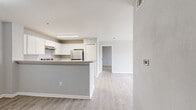 This single-floor, 2-bedroom, 3-bathroom residence offers a thoughtfully designed layout that maximizes functionality and comfort. The open-concept living area seamlessly connects the dining room, kitchen, and living room, creating a bright and cohesive space finished with light wood-style flooring throughout. The kitchen is equipped with white shaker cabinetry, stone-look countertops, stainless steel appliances including a refrigerator and electric range, and a peninsula that provides additional counter space and a natural divider between the kitchen and living areas. The living room features a ceiling fan and sliding glass doors that open onto a private balcony with outdoor views. Both bedrooms are carpeted for comfort, with the primary bedroom offering generous proportions. The residence includes six closets distributed throughout, providing ample storage. A dedicated laundry room with hookups and a pantry add to the home's practicality. The three bathrooms feature light wood-style flooring, vanities with countertops, and neutral wall tones. A hallway connects the main living areas to the bedrooms, maintaining a clear and organized flow. The overall color palette of soft grays and whites lends the space a clean, modern ambiance.