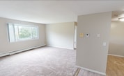 Located at 10 Wilson Road in Middletown, Rhode Island, this single-floor apartment offers 840 square feet of functional living space across two bedrooms, one bathroom, a living room, a kitchen, and a closet. The unit features neutral beige walls and wall-to-wall carpeting throughout the main living areas and bedrooms, creating a warm, cohesive aesthetic. Baseboard heating units are present in multiple rooms, ensuring consistent warmth throughout the home. The spacious living room is bathed in natural light and offers ample room for a variety of furniture arrangements. The kitchen is equipped with warm-toned wooden cabinetry, granite-style countertops, a gas range, and black appliances including a full-size refrigerator, complemented by easy-care vinyl plank flooring. The primary bedroom spans 200 square feet and features two sliding-door closets, providing generous storage, along with a window that brings in natural light. The second bedroom also benefits from natural light via a large window with outdoor views of greenery, along with a baseboard heater. The layout, as seen in the floor plan, is efficient and well-proportioned, making this apartment a practical and comfortable residence in Middletown, RI.