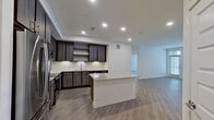 This contemporary single-floor residence is designed with a clean, modern aesthetic and a thoughtful open-concept layout. The kitchen serves as the heart of the home, showcasing dark wood cabinetry, a classic subway tile backsplash, stainless steel appliances, and a central island topped with granite countertops. Recessed lighting illuminates the space, which flows seamlessly into the open living area featuring light-toned hardwood-style flooring that runs throughout the entire residence.

The living area is bright and airy, benefiting from large windows fitted with horizontal blinds that invite natural light while maintaining privacy. A glass-paneled door provides access to the exterior, further enhancing the connection to the outdoors.

The bedrooms are generously proportioned, each featuring the same warm flooring, large windows with outdoor views, and ceiling fans for added comfort. The bathrooms are elegantly finished, with granite-topped dark wood vanities, large mirrors, and hardwood-style flooring. One bathroom includes a shower-tub combination with marble-style tile surround, while the primary bath features a dual-sink vanity and a walk-in shower.

Throughout the residence, crisp white walls, recessed lighting, and consistent high-quality finishes create a cohesive, move-in-ready environment with a modern yet welcoming atmosphere.