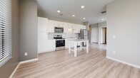 This well-appointed single-floor residence offers a clean, contemporary design with a neutral color palette and quality finishes throughout. The open-concept kitchen serves as a central hub, outfitted with crisp white shaker-style cabinetry, granite countertops, a subway tile backsplash, and a full suite of stainless steel appliances including a refrigerator, range, microwave, and dishwasher. A central kitchen island provides additional prep and dining space, while recessed lighting illuminates the room. Light wood-look luxury vinyl plank flooring extends through the kitchen and main living areas, lending a warm, cohesive aesthetic.

The bedrooms feature plush patterned carpeting and neutral gray walls, each benefiting from natural light through blinded windows that offer exterior views. The rooms are generously proportioned, providing comfortable and versatile living spaces.

The bathroom is neatly designed with a white vanity topped with granite countertops, a combination tub and shower unit with white surround, and consistent wood-look flooring that ties the space together. A wall-mounted towel bar and a wall vent add functional detail. Throughout the residence, white panel doors, brushed nickel hardware, and clean white baseboards contribute to a cohesive, move-in-ready presentation ideal for modern living.