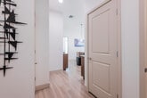 This contemporary single-floor residence offers a thoughtfully designed open-concept layout filled with natural light. The living room is a standout space, boasting floor-to-ceiling windows with transom panels above, allowing panoramic views of the surrounding neighborhood and flooding the interior with daylight. A private balcony is accessible directly from the living area, extending the space outdoors. Light hardwood flooring runs throughout the main living areas, complementing the clean, white walls and modern aesthetic.

The kitchen features warm wood-toned cabinetry with gold hardware, white countertops, stainless steel appliances, and recessed lighting — combining functionality with a refined contemporary look. Adjacent to the kitchen, the dining area includes a built-in bar cabinet with a wine cooler and open floating shelves, making it well-suited for entertaining.

The bedroom is generously sized, featuring tall ceilings, large windows with sheer curtains that invite natural light, and a ceiling fan. A walk-in closet with built-in shelving and hanging rods provides ample storage. The en-suite bathroom includes a tub-shower combination, a wood-toned vanity with a white countertop, and light hardwood flooring. A decorative hallway with modern wall art connects the spaces, adding a curated, artistic touch throughout.