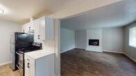 This single-floor residence offers a thoughtfully designed layout that balances comfort and functionality. The open-concept living and dining area serves as the heart of the home, highlighted by a striking white-painted brick fireplace that anchors the space. Rich, dark hardwood-style flooring runs throughout the main living areas, complemented by neutral gray walls and a textured ceiling that add warmth and character. Natural light filters in through windows with blinds, enhancing the bright, airy atmosphere.

The galley-style kitchen is efficiently laid out with abundant white shaker cabinetry featuring matte black hardware, clean white countertops, a subway tile backsplash, and black appliances including a range and refrigerator. Light wood-tone flooring ties the kitchen together seamlessly.

A connecting area leads to the bedrooms, which are finished with plush neutral carpeting, large windows overlooking lush greenery, and mirrored sliding closet doors that enhance the sense of space. A ceiling fan adds practical comfort to one of the rooms.

The full bathroom is clean and modern, featuring a white vanity with a single sink, a full tub-shower combination, and wood-tone flooring that carries a cohesive design throughout the home.
