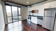 Located at 624 Yale Ave N in Seattle's South Lake Union neighborhood, this single-floor unit showcases a thoughtfully designed open-concept layout that blends modern finishes with industrial-inspired character. The exposed concrete ceiling and visible ductwork lend an urban loft aesthetic, while rich, dark hardwood floors provide a warm contrast throughout the space.

The kitchen is a central highlight, featuring crisp white cabinetry with ample storage, stainless steel appliances including an electric range with overhead microwave, a dishwasher, and a double-basin sink with a contemporary faucet. Dark countertops complement the overall modern palette, offering both style and functionality.

Expansive floor-to-ceiling windows flood the interior with natural light and frame views of the surrounding Seattle cityscape, creating a bright and airy atmosphere. The open layout allows the kitchen and living areas to flow seamlessly, maximizing the sense of space.

This unit's design strikes a balance between sleek contemporary finishes and raw industrial elements, making it a distinctive and functional urban residence. Its location in South Lake Union places it within close proximity to major tech campuses, dining, and waterfront amenities.