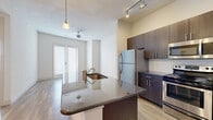 This well-appointed one-bedroom, one-bathroom residence offers thoughtfully designed single-floor living with modern finishes throughout. The open-concept kitchen serves as a focal point, featuring dark espresso cabinetry, granite countertops, a peninsula island with an undermount sink and pendant lighting, white subway tile backsplash, and a full suite of stainless steel appliances including a refrigerator, range, and microwave. Track lighting complements the kitchen's contemporary aesthetic. The living area flows naturally from the kitchen, highlighted by light hardwood-style flooring and a set of French doors that invite natural light and provide outdoor access. The bedroom offers plush carpeting, two windows with blinds, and a calm, neutral palette. The bathroom is elegantly finished with a dual undermount sink vanity, dark wood cabinetry, granite counters, a large mirror, and tile surround. A dedicated walk-in closet with wire shelving provides generous storage. An additional closet space features built-in open shelving, adding further organizational utility. A hallway connects the private spaces seamlessly, completing this efficiently designed and stylish residence.