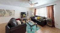 This two-story residence in Tallahassee, Florida offers a well-organized layout across two levels, providing ample living space throughout. The living room serves as the heart of the home, featuring light tile flooring, a ceiling fan with light fixture, and large windows dressed with blinds and curtains that invite generous natural light. The galley-style kitchen is outfitted with white cabinetry accented with wood trim, tile flooring, a double-basin sink, and a full suite of appliances including an electric range and dishwasher, offering practical functionality. Adjacent to the kitchen, the dining area accommodates a round glass-top table with seating for four, illuminated by track lighting and accented by a large wall art piece, creating an inviting space for meals. The bedrooms feature carpeted floors, ceiling fans, closet storage, and windows with curtains, providing comfortable and private retreats. One bedroom includes a built-in desk area, ideal as a workspace. The bathrooms are cleanly appointed with tile flooring, a tub-shower combination, and ample counter space. The two-floor layout further enhances the functional separation of living and private spaces throughout this Tallahassee home.