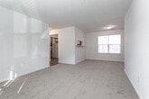 Located at 401 Jester Ct in Newport News, Virginia, this single-floor residence offers a practical and well-organized layout designed for comfortable everyday living. The open living area is finished with neutral-toned wall-to-wall carpeting and features a textured ceiling, along with blinds-covered windows that allow natural light to filter throughout the space. A pass-through opening connects the living area to the kitchen, enhancing the sense of openness. The kitchen is equipped with white cabinetry trimmed in warm wood tones, ample counter space, a stainless steel sink positioned beneath a window, and includes a dishwasher. The flooring in the kitchen transitions to durable wood-look vinyl. The bedrooms continue the carpeted flooring theme and offer generous proportions, each with windows providing natural light and a textured ceiling overhead. The bathroom is thoughtfully designed with accessibility in mind, featuring safety grab bars around the tub-shower combination, a toilet, and a vanity, all set on warm wood-look vinyl flooring. A dedicated laundry room provides washer and dryer hookups, overhead wire shelving for storage, and matching wood-look vinyl flooring, adding to the home's everyday functionality.