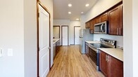 This single-floor residence offers a thoughtfully designed layout encompassing two bedrooms, two bathrooms, a kitchen, and a dedicated dining area. The kitchen serves as a central hub of the space, featuring rich medium-toned cabinetry, light countertops, stainless steel appliances including a refrigerator, range, and microwave, and recessed lighting overhead. A peninsula with an undermount sink and a pendant light above creates a natural transition into the dining area, making it ideal for both everyday meals and entertaining.

The bedrooms are carpeted and bathed in natural light through large windows that frame outdoor views of trees and the surrounding neighborhood. Each bedroom includes closet space, with at least one featuring a walk-in closet with built-in shelving and hanging rods. The neutral wall tones and rich wood-toned baseboards provide a clean, cohesive aesthetic throughout.

Both bathrooms are finished with wood-look plank flooring, warm cabinetry with light countertops, undermount sinks, and a bathtub-shower combination. The overall ambiance of the residence is modern and clean, with consistent finishes tying each room together into a functional and comfortable living environment.