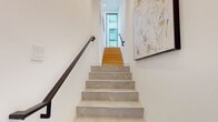 Located in the Mid City neighborhood of Los Angeles, this contemporary three-story home showcases a refined modern design with high-quality finishes throughout. The multi-level layout is connected by a striking staircase featuring marble-look tile treads, warm wood upper steps, sleek matte black metal railings, and curated wall art that sets an elevated tone from the moment you enter.

The kitchen is a standout centerpiece, outfitted with crisp white shaker cabinetry, a large quartz-topped island with dark contrasting base, a mosaic tile backsplash, and matte black pendant lighting. Light wood flooring flows throughout the main living areas, complementing the bright, white-walled interiors and large black-framed windows that invite abundant natural light.

The living area features floor-to-ceiling windows overlooking an outdoor balcony, creating a seamless indoor-outdoor connection. Bedrooms are serene and well-appointed, with built-in wood-paneled wardrobe storage and recessed lighting. Bathrooms are cleanly designed with glass-enclosed showers, tile flooring, and modern matte black fixtures — one featuring a full soaking tub. The overall ambiance is contemporary, warm, and thoughtfully detailed throughout all three levels.
