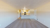 Located at 2301 North Wilbur Road in Spokane, WA, Unit 106 is a single-floor residence offering a functional and comfortable layout. The spacious living area features plush carpeting, a textured ceiling, a wall-mounted heating and cooling unit, and a large multi-pane window that fills the room with natural light and views of the surrounding landscape.

The living space opens toward a well-appointed kitchen, accessible via a breakfast bar that creates a semi-open connection between the two areas. The galley-style kitchen is equipped with white cabinetry, marble-look countertops, black appliances including an electric range and over-the-range microwave, a sink, and light wood-look flooring. A pantry or utility closet is accessible directly from the kitchen.

The bedroom is generously sized with soft carpeting and a sliding glass door leading to a private patio, offering additional natural light and outdoor access. The full bathroom includes a tub and shower combination, a white vanity with marble-look countertop, and light wood-look flooring, providing a clean and practical finish. Throughout the unit, neutral wall tones and consistent finishes create a cohesive and move-in ready atmosphere.