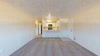 Located at 2301 North Wilbur Road in Spokane, WA, Unit 106 is a single-floor residence offering a functional and comfortable layout. The spacious living area features plush carpeting, a textured ceiling, a wall-mounted heating and cooling unit, and a large multi-pane window that fills the room with natural light and views of the surrounding landscape.

The living space opens toward a well-appointed kitchen, accessible via a breakfast bar that creates a semi-open connection between the two areas. The galley-style kitchen is equipped with white cabinetry, marble-look countertops, black appliances including an electric range and over-the-range microwave, a sink, and light wood-look flooring. A pantry or utility closet is accessible directly from the kitchen.

The bedroom is generously sized with soft carpeting and a sliding glass door leading to a private patio, offering additional natural light and outdoor access. The full bathroom includes a tub and shower combination, a white vanity with marble-look countertop, and light wood-look flooring, providing a clean and practical finish. Throughout the unit, neutral wall tones and consistent finishes create a cohesive and move-in ready atmosphere.