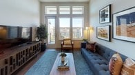 Located at 201 E Mississippi Ave in Denver's vibrant Washington Park neighborhood, this contemporary single-floor residence offers a thoughtfully designed layout with modern finishes throughout. The open-concept kitchen is a standout feature, showcasing two-tone cabinetry with warm wood upper cabinets and slate-blue lower units, stainless steel appliances including a French door refrigerator, a built-in wine cooler, a marble-look backsplash, and a generous island with quartz countertops and bar seating — ideal for both everyday cooking and entertaining. The living area is bathed in natural light through a striking bank of oversized windows and a glass door, creating a bright, airy atmosphere with views of the surrounding neighborhood. Rich hardwood flooring flows throughout the main living spaces, grounding the contemporary aesthetic. The bedrooms offer comfortable retreats, each with hardwood floors, ample natural light, and thoughtful details such as built-in shelving niches. The bathrooms are finished with large-format marble-look porcelain tile covering both the floors and walk-in shower surrounds, complemented by a sleek vanity with a white countertop and modern brushed-nickel hardware. The overall ambiance is clean, modern, and inviting — a well-appointed Denver residence designed for comfortable urban living.