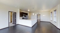 This single-floor space showcases a thoughtfully designed open-concept layout that seamlessly connects the kitchen and living areas. The kitchen is a standout feature, boasting dark espresso cabinetry that contrasts beautifully with the crisp white quartz countertops. A spacious kitchen island with an integrated sink serves as both a functional workspace and a natural gathering point, complemented by sleek pendant lighting overhead. Stainless steel appliances, including a refrigerator, microwave, and range, complete the modern culinary setup.

The rich, dark hardwood flooring flows continuously throughout the space, adding warmth and sophistication to the clean, contemporary aesthetic. Neutral white walls and smooth ceilings amplify the sense of openness, while recessed and overhead light fixtures ensure the space is well-lit throughout. A chandelier-style light fixture adds an elegant touch to the dining or living area.

Multiple doorways lead to additional rooms beyond the main living space, suggesting a well-organized floor plan with private areas for rest and convenience. The overall ambiance is modern, clean, and functional — ideal for those who appreciate a streamlined, contemporary living environment.