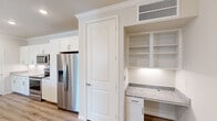 This thoughtfully designed 2-bedroom, 2-bathroom single-floor residence offers a clean, modern aesthetic throughout. The kitchen serves as the heart of the home, showcasing white shaker cabinetry, a tile backsplash, granite countertops, and a large central island with an undermount sink. Stainless steel appliances, including a French door refrigerator, range, and microwave, complete the space, while elegant pendant lighting and recessed fixtures add warmth. A built-in desk nook with open shelving provides a convenient workspace adjacent to the kitchen. Crown molding and durable wood-look flooring carry through the main living areas, lending a polished, cohesive feel. Both bedrooms are carpeted and filled with natural light from large windows with blinds. The primary bedroom features a ceiling fan and direct access to a spacious walk-in closet lined with wire shelving systems. The en-suite primary bathroom offers a granite-topped vanity, wood-look flooring, and a glass-enclosed shower. The second bathroom includes a subway-tiled tub-shower combination. A hallway connects the two bedrooms and two closets, ensuring a functional and efficient floor plan throughout this well-finished residence.