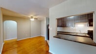 This single-floor residence at 707 N 25th St in Reading, PA offers a practical and well-maintained layout highlighted by warm hardwood flooring that extends throughout the living, dining, and bedroom areas. The open-concept living and dining space is generously sized, featuring neutral gray walls, clean white baseboards, and a ceiling fan with integrated lighting that adds both function and comfort. A pass-through peninsula connects this area to the kitchen, which is equipped with rich dark wood cabinetry, a white subway tile backsplash, granite-style countertops, and black appliances including a full-size refrigerator, range, and microwave. Under-cabinet lighting adds practicality to the kitchen's efficient galley-style layout. The bedroom offers a comfortable footprint with a wall-mounted air conditioning unit and a window that allows natural light and outdoor views. The bathroom features white tile wainscoting, tile flooring, and a full tub and shower combination with chrome fixtures and a grab bar. A hallway connects the rooms, contributing to a straightforward and functional floor plan throughout the space.