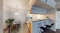 This single-story residence offers a well-organized layout that maximizes functionality and comfort. The heart of the home is an open-concept kitchen and dining area, seamlessly connected by a peninsula-style breakfast bar with a dark granite-look countertop and bar seating. The galley kitchen is efficiently designed with ample white cabinetry accented by warm wood trim, gray countertops, light tile flooring, and a full suite of white appliances including a refrigerator, electric range, and built-in microwave. Crown molding and an elegant chandelier enhance the adjoining dining area, which features warm wood-look flooring that flows throughout the living spaces. The bedroom is a bright, restful retreat, benefiting from a large window that invites natural light and offers views of greenery outside. It is complemented by a ceiling light fixture and rich, dark hardwood-style flooring. The full bathroom includes a single vanity with a cabinet mirror, gray countertops, a shower-tub combination, and convenient access to a walk-in closet outfitted with shelving and hanging storage. Together, these spaces create a practical and inviting single-floor living environment.