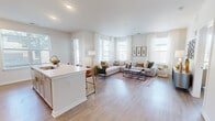 This thoughtfully designed 1-bedroom, 2-bathroom residence offers a bright and functional layout finished with light hardwood-style flooring and a clean, neutral color palette throughout. The open-concept kitchen and living area forms the heart of the home, where a sleek white kitchen island with bar seating flows seamlessly into the spacious living room. The kitchen is equipped with stainless steel appliances, white shaker cabinetry, and a undermount sink, while the adjacent living area benefits from large bay windows dressed with sheer curtains that invite abundant natural light. Two dedicated office spaces provide versatile options for remote work or flex use, each featuring windows with exterior views. The primary bedroom is a comfortable retreat with a generous walk-in closet outfitted with multi-level wire shelving, complemented by a second closet space for additional storage. Both bathrooms are finished with white subway tile surrounds, white vanity cabinetry, and light countertops. A clean hallway connects the private areas of the home, maintaining a well-organized flow between spaces. Throughout the residence, the consistent use of light tones, recessed lighting, and wide-plank flooring creates a cohesive and welcoming ambiance.