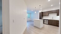 Located at 232 E 2nd St in the heart of Los Angeles, this modern one-bedroom, one-bathroom unit offers a well-designed layout with contemporary finishes throughout. The open-concept living and kitchen area is anchored by a sleek kitchen featuring rich dark-brown cabinetry, white quartz countertops, a central island, and a full suite of stainless steel appliances including a gas range, microwave, dishwasher, and refrigerator. Pendant lighting and recessed fixtures illuminate the space, while light wood-style flooring adds warmth and continuity across the main living areas. The bedroom is a comfortable, quiet retreat finished with plush carpeting and a window with blinds that allows in natural light. It connects directly to a spacious walk-in closet outfitted with multiple hanging rods and built-in shelving, providing ample storage. The bathroom is clean and functional, featuring tile flooring, a tiled shower-tub combination, and a minimalist design consistent with the rest of the unit. Crisp white walls and clean lines throughout give the space a bright, modern aesthetic suited to contemporary urban living in Downtown Los Angeles.