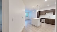 Located at 232 E 2nd St in the heart of Los Angeles, this modern one-bedroom, one-bathroom unit offers a well-designed layout with contemporary finishes throughout. The open-concept living and kitchen area is anchored by a sleek kitchen featuring rich dark-brown cabinetry, white quartz countertops, a central island, and a full suite of stainless steel appliances including a gas range, microwave, dishwasher, and refrigerator. Pendant lighting and recessed fixtures illuminate the space, while light wood-style flooring adds warmth and continuity across the main living areas. The bedroom is a comfortable, quiet retreat finished with plush carpeting and a window with blinds that allows in natural light. It connects directly to a spacious walk-in closet outfitted with multiple hanging rods and built-in shelving, providing ample storage. The bathroom is clean and functional, featuring tile flooring, a tiled shower-tub combination, and a minimalist design consistent with the rest of the unit. Crisp white walls and clean lines throughout give the space a bright, modern aesthetic suited to contemporary urban living in Downtown Los Angeles.