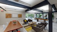 The Schoettler Village Community Room and Fitness Center in Chesterfield, Missouri, is a single-story amenity facility defined by its industrial-modern architectural design. Exposed steel beams and corrugated metal ceilings span the open interior, creating a bold visual framework complemented by bright, energy-efficient linear lighting throughout.

The community room serves as a versatile gathering space, furnished with multiple seating arrangements including lounge chairs, sofas, and dining-height tables with colorful accent chairs. A kitchenette area features gray cabinetry, a sink, a beverage cooler, and a wall-mounted flat-screen TV set against a striking wood-planked accent wall. Large glass doors flood the space with natural light and open directly to an outdoor pool area, seamlessly connecting interior and exterior.

The fitness center is comprehensively equipped with TRUE-brand cardio machines, including treadmills and stationary bikes, alongside a full selection of strength training equipment and free weights. A dedicated studio room with dark hardwood floors, floor-to-ceiling mirrors, and a mounted display screen provides space for flexible group or individual workouts. Herringbone-patterned carpet tiles throughout the fitness areas add a refined, contemporary touch to the overall athletic environment.