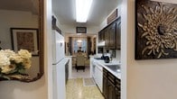 Located at 7 Elk Drive in Monticello, New York, this single-floor 1-bedroom, 1-bathroom residence offers a comfortable and thoughtfully arranged living space. The galley-style kitchen is a standout feature, showcasing rich, dark wood cabinetry with decorative hardware, light stone-patterned countertops, and white appliances including a gas range, dishwasher, and full-size refrigerator. Overhead, a bright skylight-style flush fixture keeps the kitchen well-lit, while the tile flooring adds a classic, easy-to-maintain surface underfoot. The kitchen flows naturally into a dedicated dining area, which is bathed in natural light from a large window dressed with elegant dark curtains. A decorative pendant light hangs above the dining table, creating a warm and intimate ambiance. The space is accented with personalized wall décor and carefully chosen furnishings that lend a homey, lived-in character throughout. The overall layout is efficient and practical, making excellent use of the available space on a single level. With its charming details and welcoming atmosphere, this residence offers a cozy retreat in the heart of Monticello, NY.