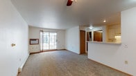 This single-floor unit offers a clean, functional layout designed for comfortable everyday living. The spacious main living area is carpeted throughout and features a ceiling fan, a wall-mounted air conditioning unit, and a sliding glass door that floods the room with natural light and provides access to an outdoor area. A baseboard heating system runs along the perimeter, ensuring year-round comfort. The open layout connects seamlessly to a half-wall pass-through that frames the kitchen, creating an airy, connected feel between the living and cooking spaces.

The galley-style kitchen is efficiently designed with ample cream-toned cabinetry on both sides, wood-look flooring, a double-basin stainless steel sink, a coil-top electric range, a refrigerator, and a dishwasher — offering all essential appliances in a compact, organized footprint.

The bathroom is bright and well-lit, featuring a wide vanity with white cabinetry and generous counter space, a large mirror, a full tub-shower combination, and matching wood-look flooring that ties in with the kitchen.

The bedroom is generously sized with soft carpet, a ceiling fan with light fixture, and a wide reach-in closet with built-in shelving and hanging rods, providing practical storage solutions. The overall aesthetic is neutral and move-in ready.