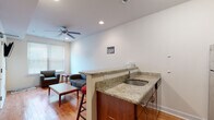 This single-floor unit offers a practical, well-organized layout designed for comfortable living. The living area is bright and welcoming, featuring warm hardwood flooring, recessed lighting, and a ceiling fan that contribute to an airy atmosphere. Natural light filters in through blinds-fitted windows, enhancing the open feel of the space. A built-in wet bar with granite countertops and an undermount sink serves as a functional divider between the living and kitchen areas, adding a convenient amenity for daily use.

The kitchen is efficiently designed with rich, dark wood cabinetry, granite countertops, and a full suite of stainless steel appliances, including an electric range with oven, over-the-range microwave, and a refrigerator. The hardwood flooring continues seamlessly into this space, maintaining visual consistency throughout.

The bedroom is a quiet, simply finished room with hardwood floors and a window providing natural light. The bathroom is clean and straightforward, featuring white tile flooring, a full bathtub with tiled surround, a toilet, and a vanity with matching dark wood cabinetry. The overall ambiance of the unit is neutral and functional, with white walls providing a clean, adaptable backdrop throughout.
