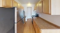 This single-floor unit presents a straightforward, functional layout spread across several well-defined areas. The living room is generously proportioned, finished with light wall-to-wall carpeting and neutral walls that create a bright, open atmosphere. A large sliding glass door fitted with vertical blinds allows substantial natural light to fill the space while providing access to an outdoor view. A partial wall divides the living area from the kitchen, maintaining an open connection between the two spaces.

The galley-style kitchen is efficiently designed, featuring light wood cabinetry with ample upper and lower storage, granite-tone countertops, and durable wood-look flooring. Stainless steel appliances, including a full-size refrigerator and an electric range with a ventilation hood, complete the kitchen's practical setup.

The bedroom offers a comfortable, carpeted space with a reach-in closet equipped with a built-in shelf and rod, accessible via bifold doors. A door from the bedroom leads conveniently toward the rest of the unit.

The full bathroom is finished with white square wall tile, tile flooring, and a single-sink vanity with wood cabinetry. A combined tub and shower with white tile surround includes grab bars, adding accessibility. A large mirror with overhead lighting completes the space.