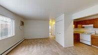 This single-floor unit offers a practical and functional layout across several well-defined spaces. The living area is generously sized, featuring neutral wall-to-wall carpeting, crisp white walls, and a large window dressed with vertical blinds that allows natural light to fill the room. A baseboard heating system runs along the perimeter, and a wall-mounted air conditioning unit provides climate control year-round. A built-in closet with double doors adds convenient storage directly off the living space.

The kitchen is positioned adjacent to the living area in an open-access layout. It features warm-toned wood cabinetry, light countertops, tile flooring, and white appliances including an electric range and a full-size refrigerator. An overhead range hood is installed above the stove for ventilation.

Both bedrooms are carpeted and maintain the same clean, neutral aesthetic found throughout the unit. Each room is equipped with a ceiling fan and a window with vertical blinds, as well as baseboard heating. The rooms offer a comfortable sense of space suitable for standard bedroom furnishings.

The bathroom is finished with earthy tile flooring and features a full-size bathtub with a shower, a toilet, and chrome hardware accents, presenting a clean and functional design throughout.