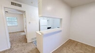 This single-floor, one-bedroom, two-bathroom unit offers a practical and well-organized layout designed to maximize every square foot of its compact footprint. The combined kitchen and living area forms the heart of the unit, where a pass-through counter with a white laminate surface visually connects the kitchen to the carpeted living space, promoting an open feel. The kitchen is outfitted with white cabinetry, a coil-burner electric range, a full-size refrigerator, and a stainless steel sink beneath a window that brings in natural light. A multicolored tile floor adds a subtle decorative touch to the kitchen area.

The bedroom is a well-proportioned, carpeted room with a ceiling fan and light fixture, and benefits from direct access to a private bathroom featuring a tiled tub-shower surround. A generous walk-in closet adjoins the bedroom, featuring built-in shelving and hanging rods on hardwood-style flooring, providing ample storage. A second bathroom and a dedicated utility room with washer and dryer hookups add further practicality to the layout. Throughout the unit, white walls and neutral carpeting create a clean, bright aesthetic that is easy to personalize.