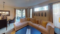 This single-floor residence offers a thoughtfully designed layout with a variety of comfortable living spaces. The main living room is a welcoming area anchored by a large sectional sofa accented with warm-toned pillows and decorative wall art. Large arched windows and glass doors flood the room with natural light and provide direct access to a private outdoor balcony, offering relaxing outdoor views surrounded by lush greenery.

The kitchen features light wood cabinetry, tile flooring, a full suite of appliances including a refrigerator and electric range, ample counter space with a breakfast bar overhang, and a double-basin sink. Adjacent to the kitchen, the dining area includes an elegant pendant light fixture overhead and flows seamlessly into the living spaces.

The primary bedroom is generously sized with plush carpeting, track lighting, dual windows with draped curtains, and a walk-in closet. A second, versatile room with carpet and a closet offers flexibility as a guest bedroom or sitting room. Both bathrooms are outfitted with full tub-shower combinations, white cabinetry, and neutral tile finishes.

Throughout the residence, a warm, neutral color palette and consistent styling create a cohesive and inviting ambiance suited for comfortable everyday living.