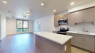This single-floor residence in Berkeley, CA offers a thoughtfully designed open-concept layout with contemporary finishes throughout. The kitchen serves as a central highlight, featuring stainless steel appliances including a range, microwave, and refrigerator, complemented by flat-front cabinetry in a warm taupe finish, white quartz countertops, a tile backsplash, and a large island that flows seamlessly into the living area. Wood-look flooring runs through the main living spaces, enhancing the modern aesthetic, while recessed lighting and track lighting provide well-distributed illumination.

The living area benefits from natural light through large windows with views of surrounding greenery. Two bedrooms are carpeted for comfort, each featuring black-framed windows that invite ample daylight and neighborhood views. The unit includes two full bathrooms, both finished with wood-toned vanities, white quartz counters, brushed nickel fixtures, and tub-shower combinations. A dedicated in-unit laundry closet with a stacked washer and dryer adds everyday convenience. The overall design is clean, neutral, and move-in ready, reflecting a cohesive modern sensibility throughout.