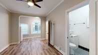 Located in the heart of Hollywood at 1733 N Cherokee Ave, this single-floor unit combines classic architectural character with clean, updated finishes throughout. The main living area is bright and welcoming, showcasing warm hardwood-style plank flooring, crisp white crown molding, and neutral taupe walls that create an inviting, versatile backdrop. A ceiling fan overhead provides both comfort and a subtle design accent.

A defining architectural highlight is the striking arched window that floods the space with natural light and lends a distinctive vintage charm. Paired with an adjacent standard window fitted with blinds, the living area maintains a bright and airy atmosphere. A built-in wall heater ensures year-round comfort, while a recessed electrical panel is neatly integrated into the wall.

The layout flows efficiently, with a dedicated area that accommodates a refrigerator, suggesting a compact kitchen space. The bathroom stands out with bold, classic black-and-white checkered floor tiles and matching black square wall tiles in the shower, accented by a contrasting white tile border. A white vanity with a sink and a wall-mounted mirror complete the space with clean, functional design.

The unit's single-floor layout, period-inspired details, and updated elements make it a distinctive offering in one of Los Angeles' most iconic neighborhoods.