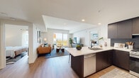This contemporary single-floor residence offers a thoughtfully designed open-concept layout that seamlessly connects the kitchen, dining, and living areas. The kitchen is a standout feature, boasting rich dark wood cabinetry that extends to the ceiling, a striking hexagonal tile backsplash, stainless steel appliances including a gas range and full-size refrigerator, and a generous island with a white quartz countertop and an undermount sink — ideal for both cooking and casual dining.

The living area is bright and airy, bathed in natural light from large sliding glass doors that open to an outdoor balcony with open views of the surrounding cityscape. Light wood-tone flooring flows consistently throughout the space, enhancing the cohesive and modern aesthetic.

The two bedrooms are comfortably sized, each featuring large windows that invite natural light and views of the outdoors. The rooms are finished with the same clean, neutral palette found throughout the residence.

The bathroom is well-appointed with dark wood cabinetry, a wide vanity with a white countertop, a large mirror, and a full tiled tub-shower combination. Recessed lighting and crisp white walls contribute to the clean, contemporary feel of the entire space.