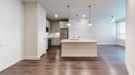 This well-appointed single-floor residence offers a thoughtfully designed open-concept layout that seamlessly connects the kitchen and living areas. The kitchen is a standout feature, centered around a large island with a granite countertop and an integrated sink, illuminated by a trio of elegant brass pendant lights. Gray shaker-style cabinetry lines the walls, complemented by a decorative mosaic tile backsplash and a full suite of stainless steel appliances, including a range, microwave, and refrigerator. Rich, dark hardwood-style flooring extends throughout the main living areas, adding warmth and contrast to the light neutral walls and white trim.

The bathroom is finished with floor-to-ceiling tile in the walk-in glass-enclosed shower and continues the same durable hardwood-style flooring. A walk-in closet is directly accessible from the bathroom, offering generous storage. The bedroom is a calm and comfortable retreat, featuring plush wall-to-wall carpeting, a ceiling fan, and a window fitted with blinds that allows for natural light while maintaining privacy. Recessed lighting throughout the main living areas ensures consistent, ambient illumination. The overall aesthetic is clean, modern, and move-in ready, with a neutral palette that provides a versatile backdrop.