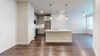 This well-appointed single-floor residence offers a thoughtfully designed open-concept layout that seamlessly connects the kitchen and living areas. The kitchen is a standout feature, centered around a large island with a granite countertop and an integrated sink, illuminated by a trio of elegant brass pendant lights. Gray shaker-style cabinetry lines the walls, complemented by a decorative mosaic tile backsplash and a full suite of stainless steel appliances, including a range, microwave, and refrigerator. Rich, dark hardwood-style flooring extends throughout the main living areas, adding warmth and contrast to the light neutral walls and white trim.

The bathroom is finished with floor-to-ceiling tile in the walk-in glass-enclosed shower and continues the same durable hardwood-style flooring. A walk-in closet is directly accessible from the bathroom, offering generous storage. The bedroom is a calm and comfortable retreat, featuring plush wall-to-wall carpeting, a ceiling fan, and a window fitted with blinds that allows for natural light while maintaining privacy. Recessed lighting throughout the main living areas ensures consistent, ambient illumination. The overall aesthetic is clean, modern, and move-in ready, with a neutral palette that provides a versatile backdrop.